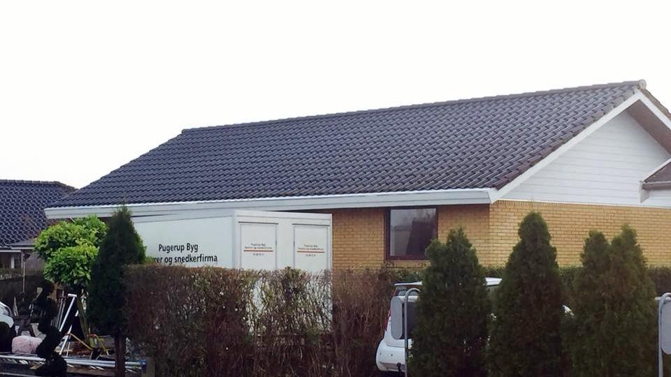 Et hus med en grå tag og en hvid lastbil parkeret foran, omgivet af buske og træer.