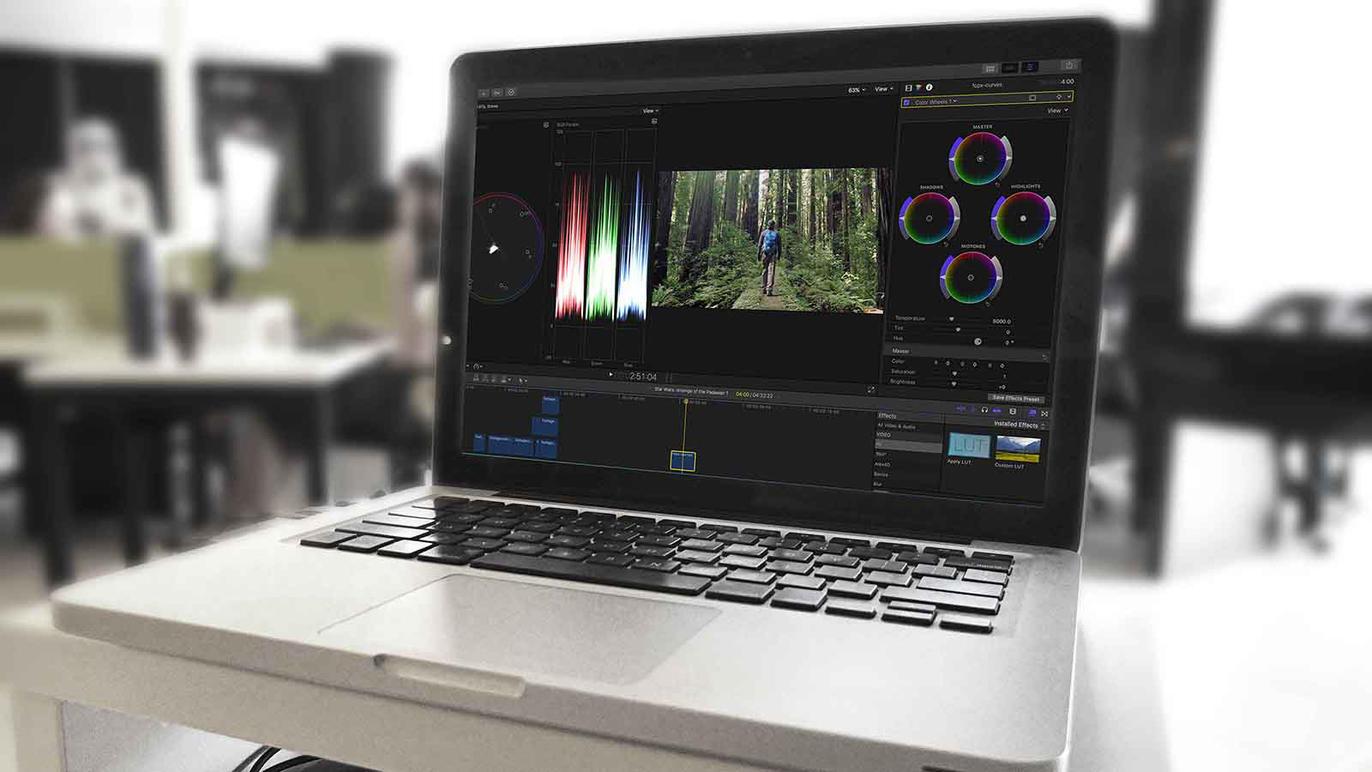 En bærbar computer viser farvekorrektion i et videoredigeringsprogram med en skovscene på skærmen.