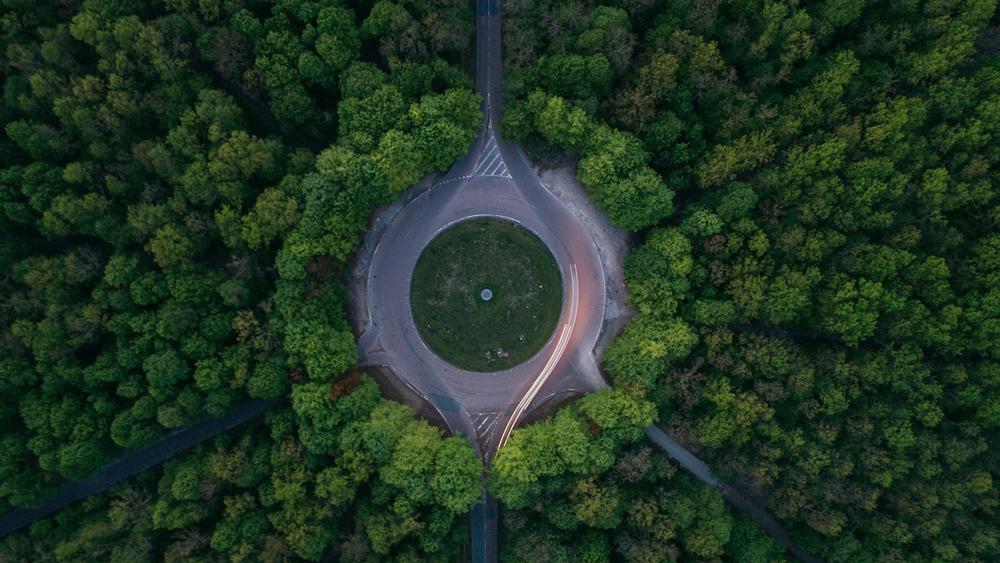 Luftfoto af en rundkørsel omgivet af tæt skov med grønne træer og veje, der fører ind og ud.