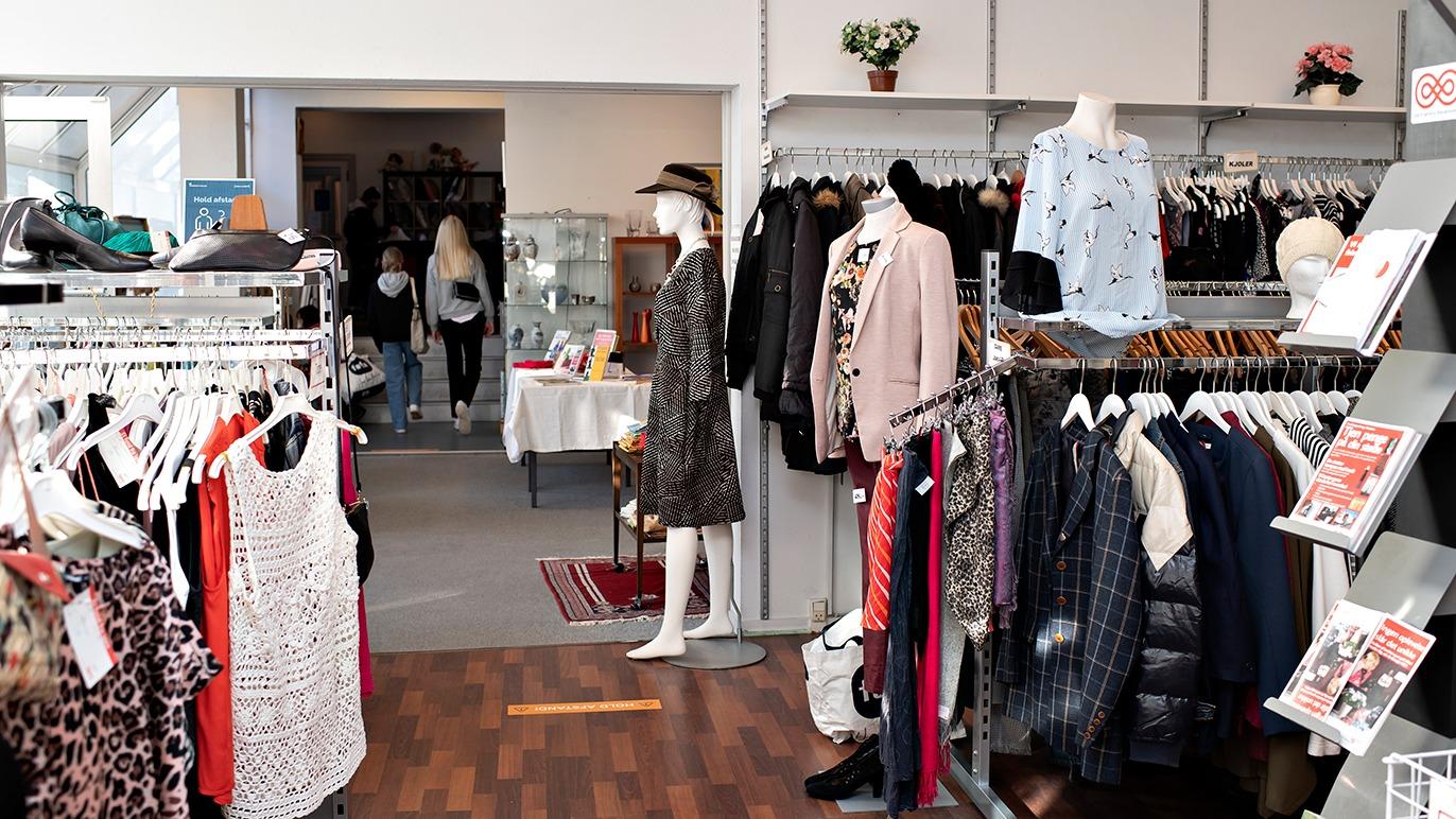 En indendørs butik med tøjstativer, mannequiner og en række forskellige beklædningsgenstande.
