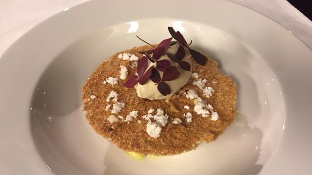 En desserttallerken med en sprød kage, flødeskum og spiselige blomster som pynt.