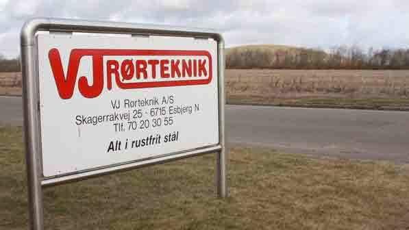 VJ Rørteknik skilt ved vejen med kontaktinformation og landskab i baggrunden.