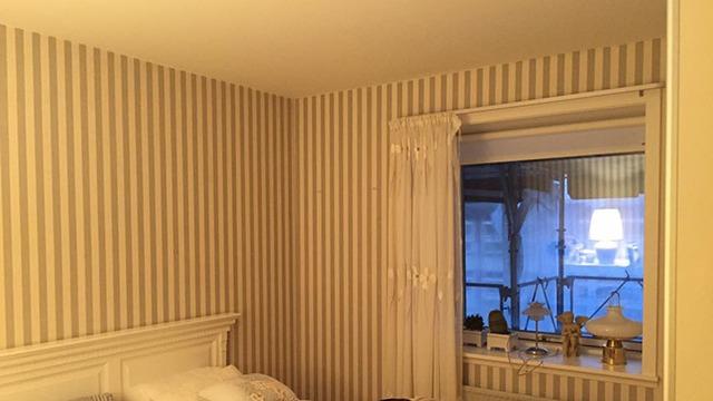 Et lyst soveværelse med stribede vægge, en seng og et vindue med gardiner.