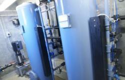 To store og cylindrisk vandbehandlingsudstyr i en teknisk installation med rør og pumper.