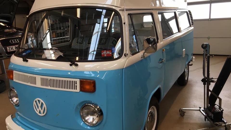En blå og hvid Volkswagen varevogn parkeret i en garage med bilværktøj i baggrunden.
