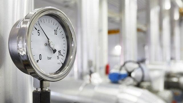 Manometer med tydelig trykmåling i en industriel setting med rør og udstyr i baggrunden.