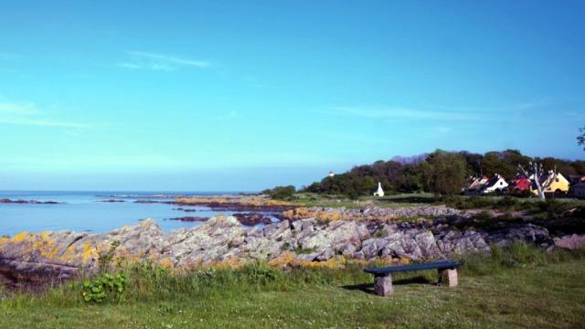 En smuk kystlinje med klipper, græs og farverige både i baggrunden under en klar blå himmel.