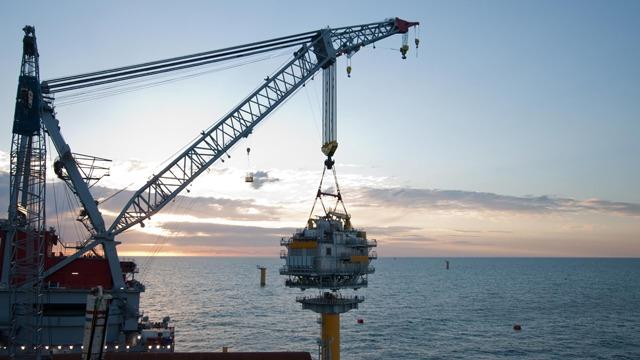 En kran løfter en offshore platform ved solnedgang over havet.