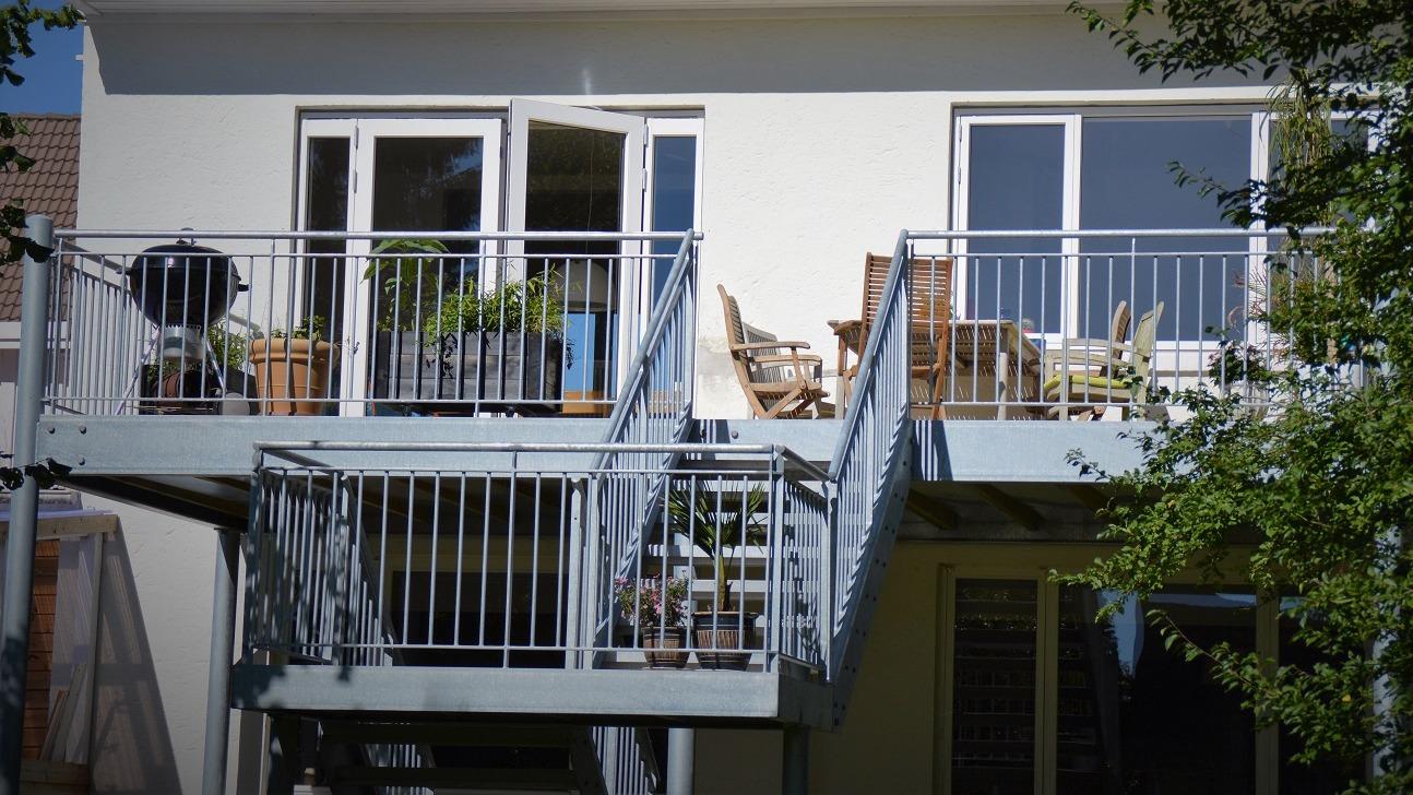 En moderne bygning med en balkon, der har møbler og planter, samt en trappe i metal.