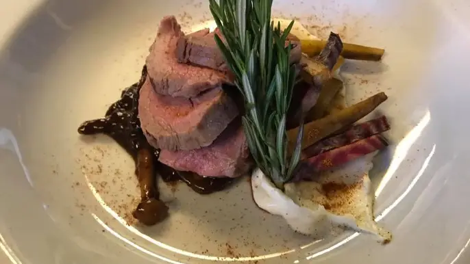 Lækkert stykke oksekød serveret med svampe, grøntsager og rosmarin på en hvid tallerken.