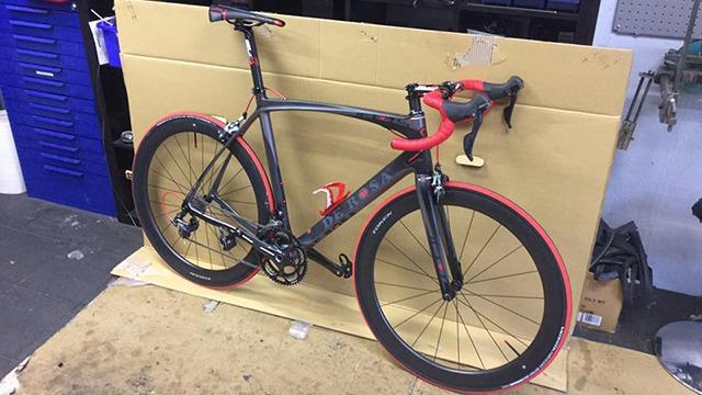 En racercykel med sort og rød ramme står på en kasse i et værksted.