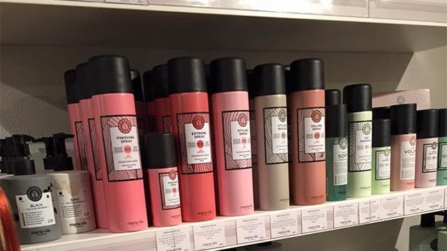 Hylder med forskellige hårplejeprodukter i farverige flasker og krukker, herunder shampoo og balsam.