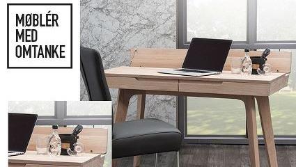 Moderne skrivebord i lys træ med laptop og kontorartikler, placeret ved vindue med marmorvæg.
