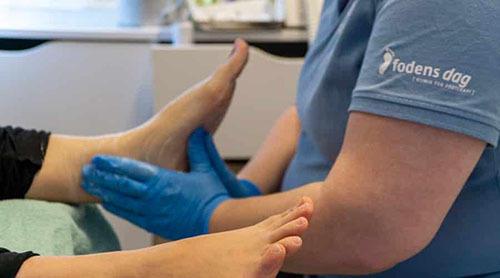 En fodbehandling, hvor en behandler masserer en klients fod iført blå handsker.