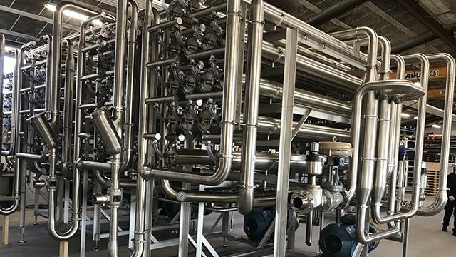 Stort rørsystem i rustfrit stål i en industriel bygning med flere ventiler og pumper.