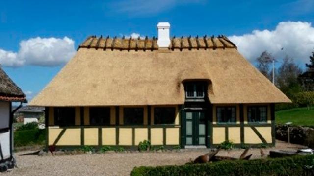 Et smukt stråtækt hus med grønne vægge og hvidt vindue under en blå himmel.