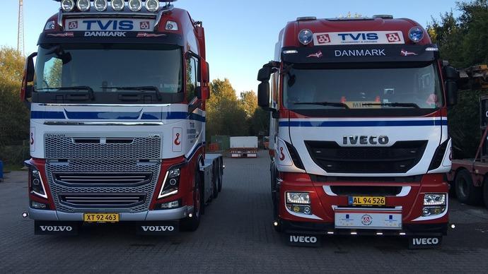 To lastbiler fra TVIS Danmark parkeret side om side, en Volvo og en Iveco, begge med logoer og nummerplader.