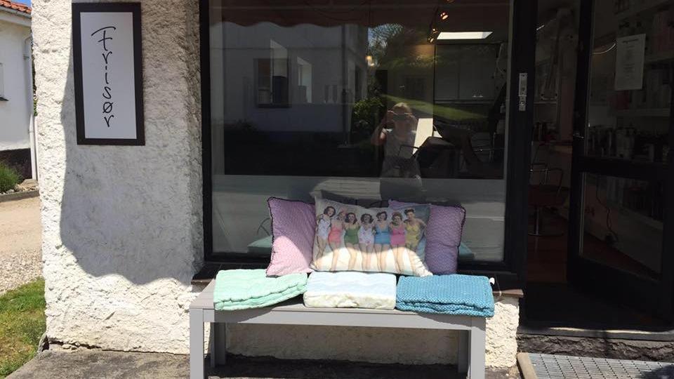 Bænk foran en butik med puder og tæpper i pastelfarver, der står ved en glasdør.