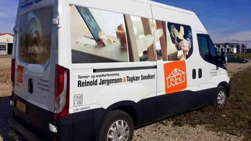 En varevogn med reklame for Reinhold Jørgensen og Tømrermester Søren. Varevognen står parkeret på en grusvej.