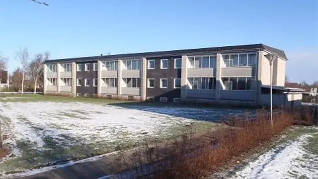 En bygning med flere etager og vinduer, omgivet af sne og græs, under en klar blå himmel.