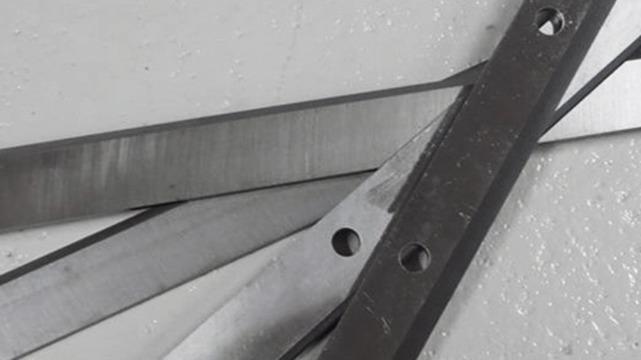 Nærbillede af metalblade i forskellige størrelser og former, der ligger oven på hinanden på en hvid overflade.