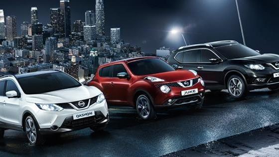 Tre Nissan biler parkeret på en vej med en by i baggrunden, herunder en hvid, en rød og en sort SUV.