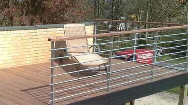 En solstol på en træterrasse med gelænder, omgivet af grønne træer og en rød bil i baggrunden.