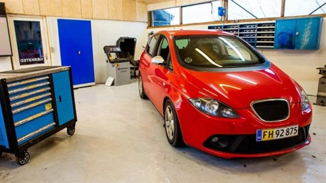 En rød bil parkeret i en garage med værktøjskasse og værktøjsreoler i baggrunden.