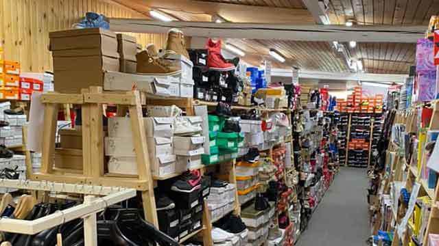 En skobutik med hylder fyldt med sko og kasser, der strækker sig langs en lang gang.