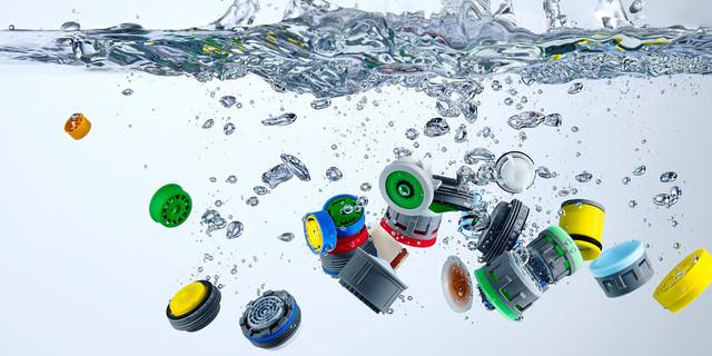 Farverige plastiklåg og kapsler, der sprøjter ind i vandet med bobler omkring dem.