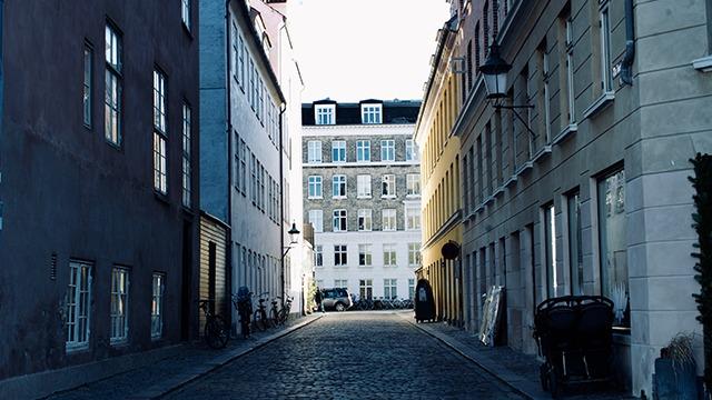 En stille gade med brosten, omkranset af bygninger i forskellige farver og stilarter i København.