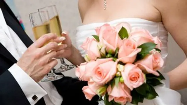 Brud med en buket lyserøde roser, mens hun skåler med champagne i et festligt miljø.