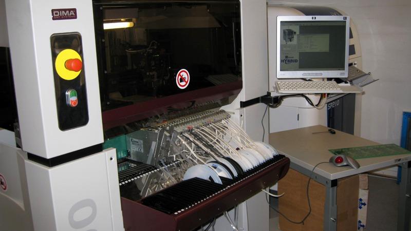 En maskine til automatiseret opvask med en computer ved siden af, der viser kontrolpanel og opvaskestativer.