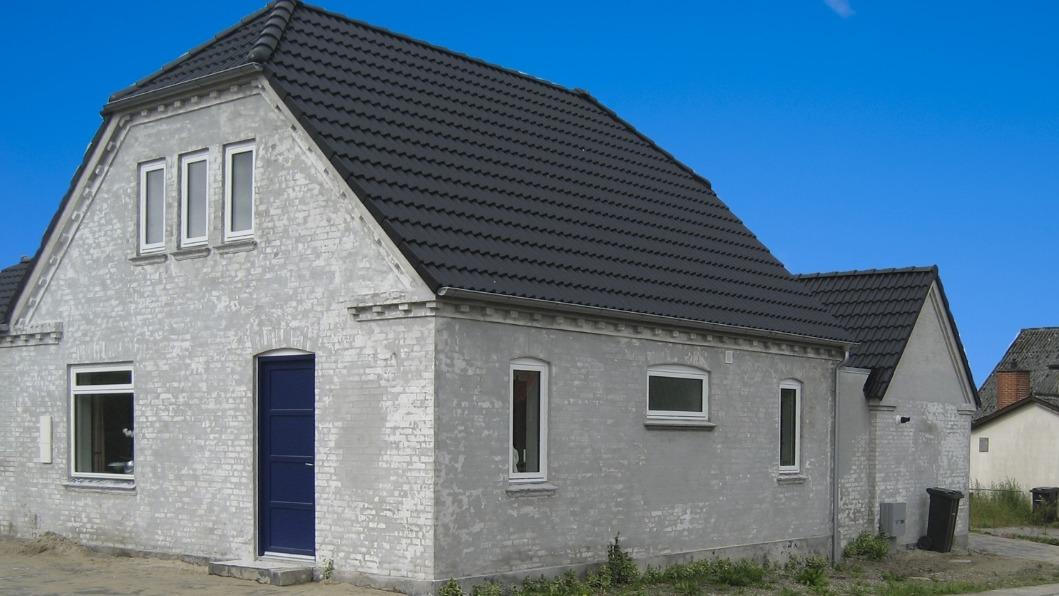 Et hvidt hus med skråtag og blå dør, beliggende i et åbent område med klar blå himmel.
