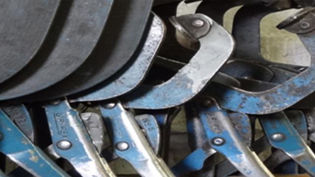 Nærbillede af metalværktøj med blå håndtag og slidte overflader, der viser detaljer i konstruktionen.