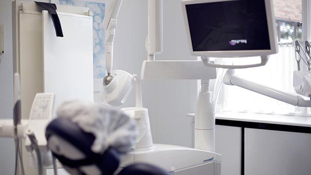 Et moderne tandlægekontor med udstyr som stol, skærm og lamper i et lyst rum.