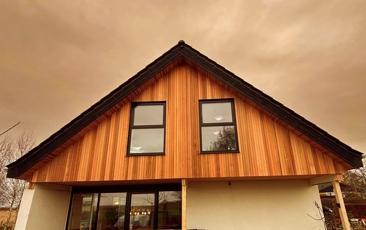 Et moderne hus med træfacade og store vinduer under en dramatisk himmel.