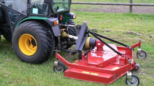En grøn traktor med en rød græsslåmaskine monteret bagpå, der står på en græsplæne.