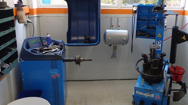Værksted med udstyr til dækmontering og afbalancering, herunder en dækafbalanceringsmaskine og værktøjsstation.
