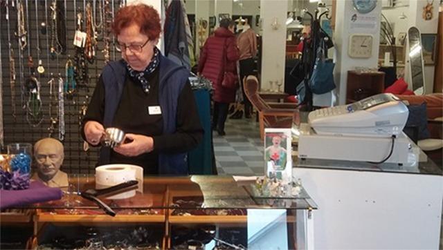 En kvinde står ved en disk i en butik, mens hun holder en skål og ser på smykker i baggrunden.