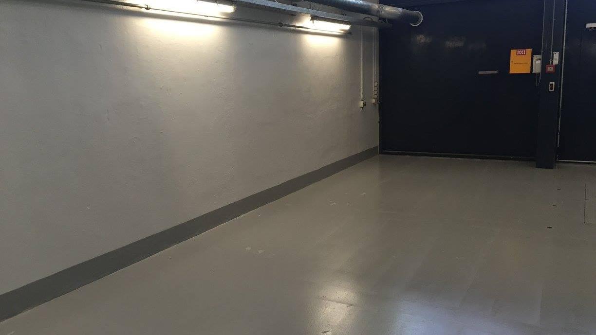Tom garage med grå vægge og lysrør, der belyser det glatte gulv.