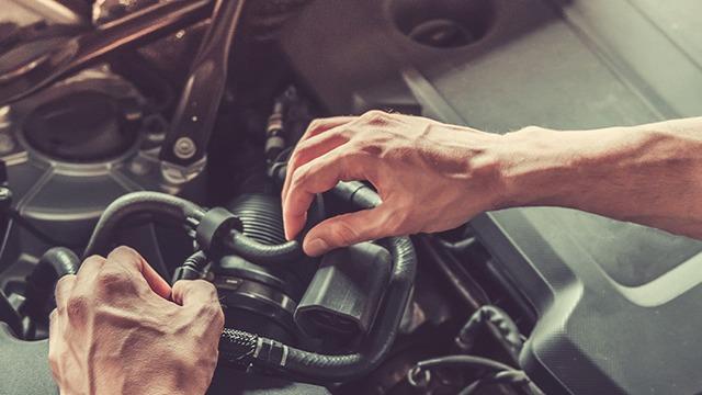 Hånd, der arbejder på motoren i en bil, mens den justerer slanger og forbindelser.