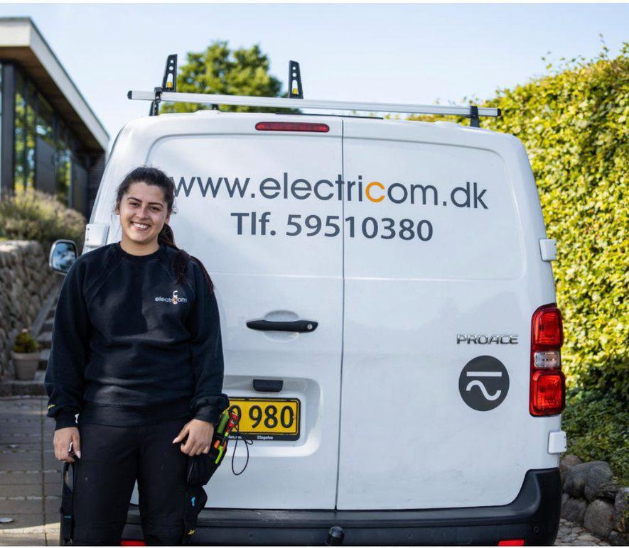 En kvinde står ved siden af en hvid varevogn med teksten "www.electricom.dk" og telefonnummeret synligt.