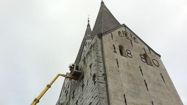 Reparationsarbejde på en kirketårn med en lift, der når op til spidserne, med årstallet 1880 synligt.