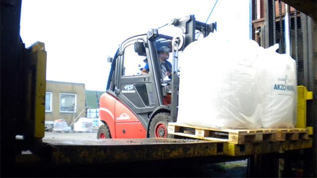 Gaffeltruck, der løfter en stor sæk på en palle i et lagerområde.