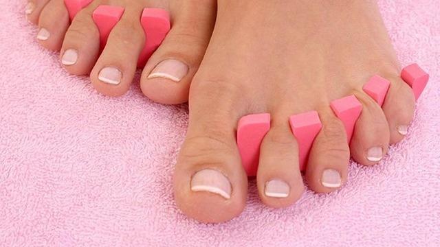 Fødder med lyserøde tåseparatorer på en blød pink håndklæde, klar til pedicure.