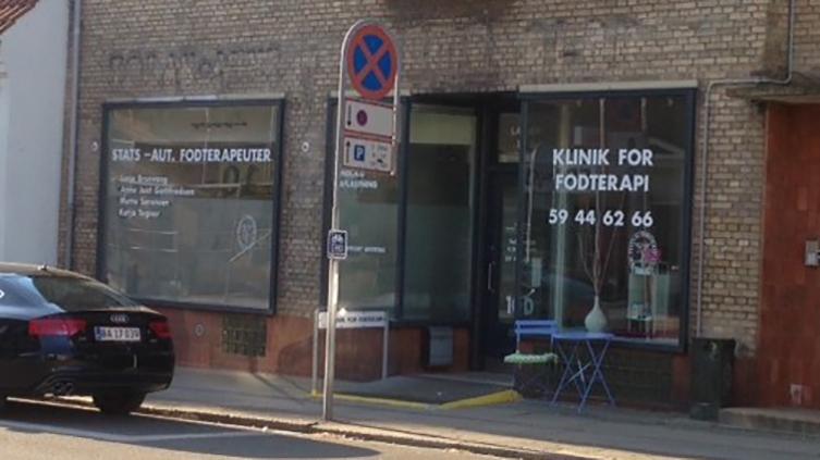 Facade af en klinik for fodterapi med store vinduer og skilt, der viser kontaktinformationer.