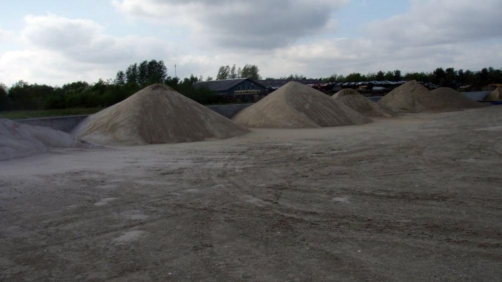 Store sand- og grusbakker på en byggeplads under en skyet himmel.