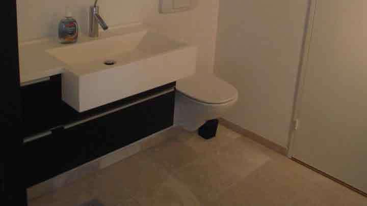 Moderne badeværelse med hvid vask, toilet og mørke skabe på væggen. Fliser på gulvet.