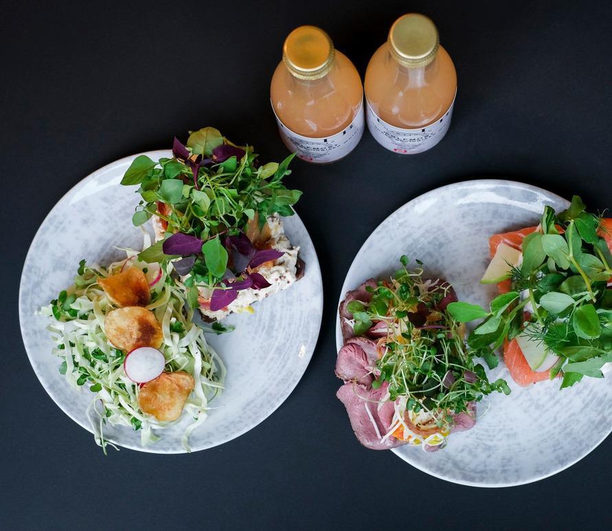 To plader med farverig salat, grøntsager og drikkevarer i glasflasker på en sort overflade.